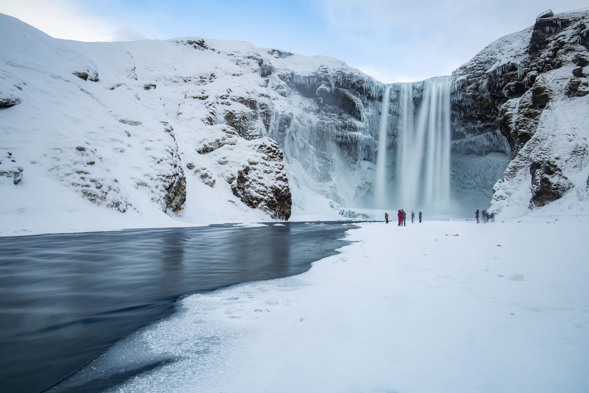 people standing at thge base of a waterfall in winter