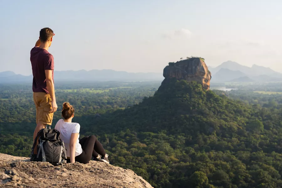 two people looking out at a large rock poking out of a forest.