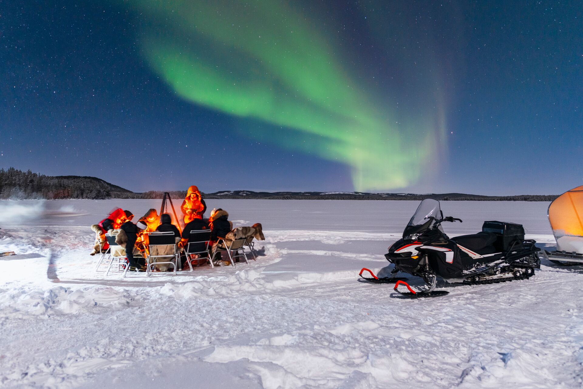 People around a fire with the northern lights above
