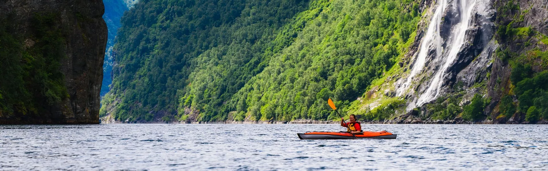 Person Kayaking in a green fjord with a waterfall