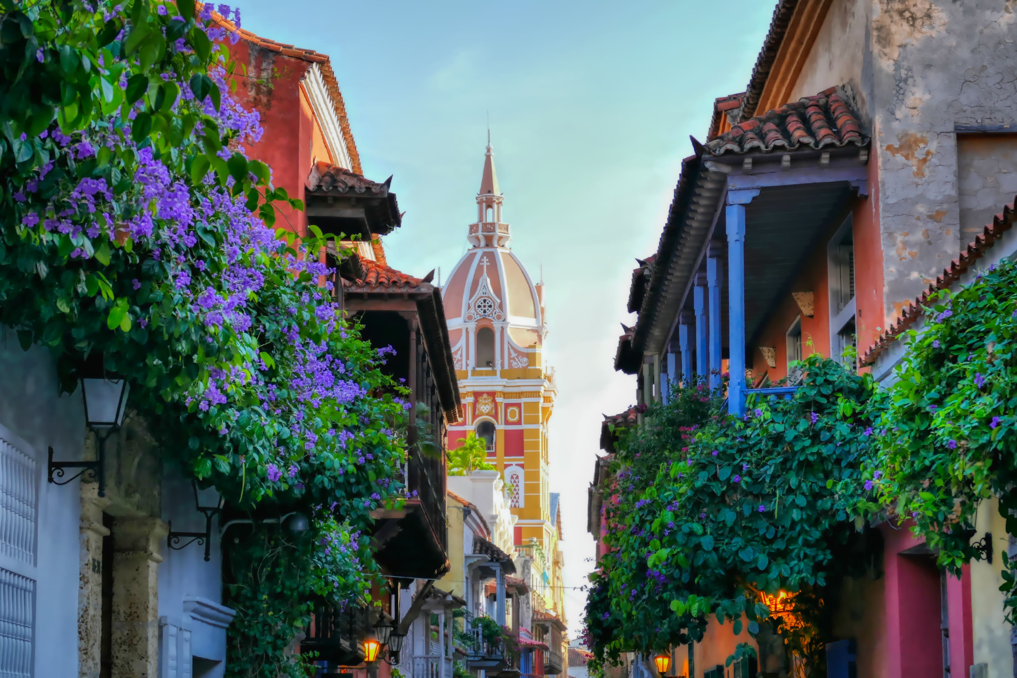 A narrow street with a church steeple in the background