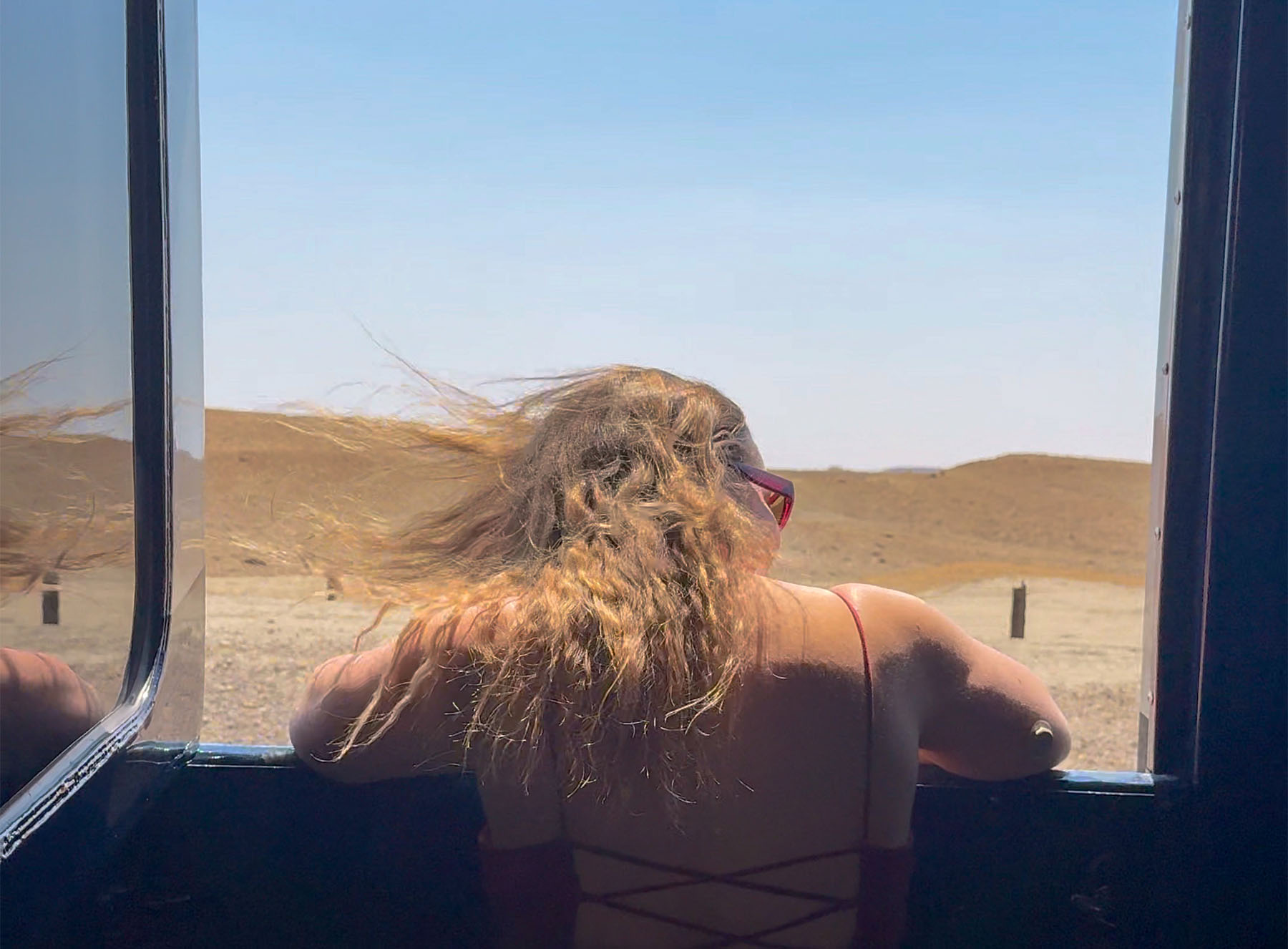 back view of a woman looking out open train car window at the scenery