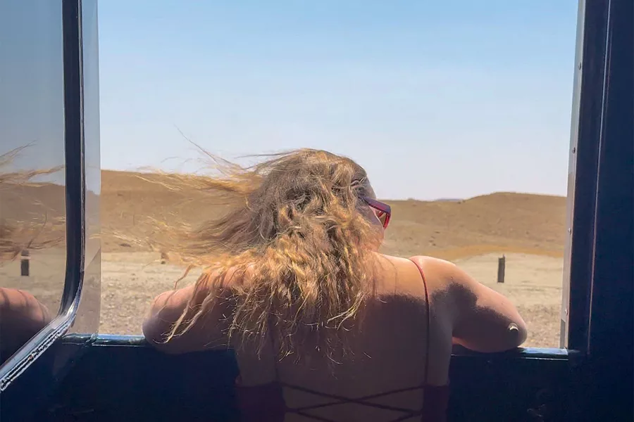 back view of a woman looking out open train car window at the scenery