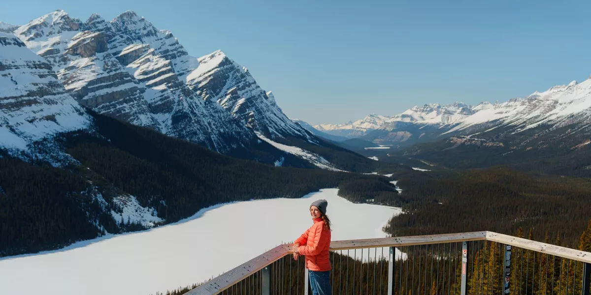 Woman smiling back with frozen lake, forest and mountains in the background