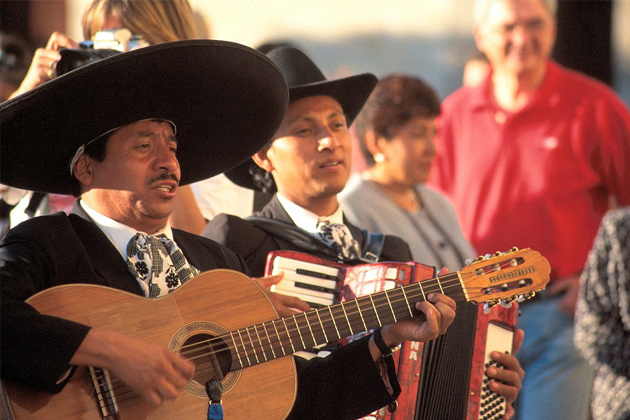 A man in a cowboy hat playing a guitar with other musicians