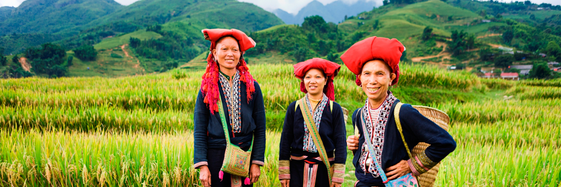 Three people in costumes standing on the grass with mountains in the background