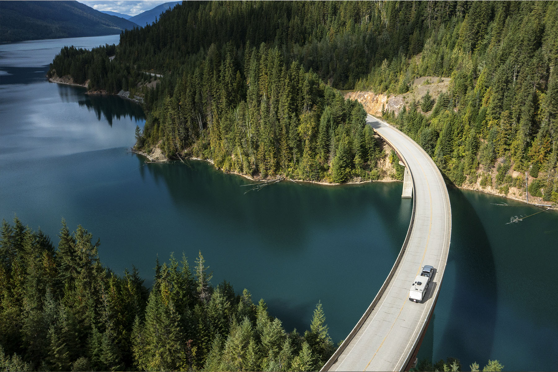 Car driving along highway over water inbetween two forested areas