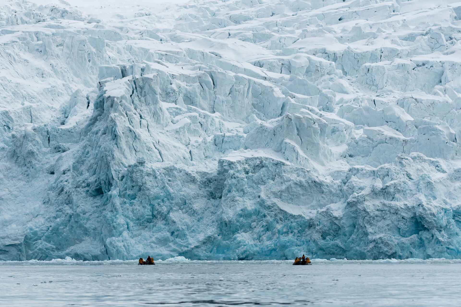 people on inflatable boats in front of a large glacier