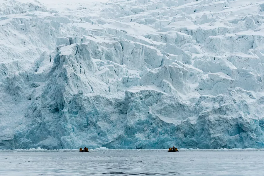 people on inflatable boats in front of a large glacier
