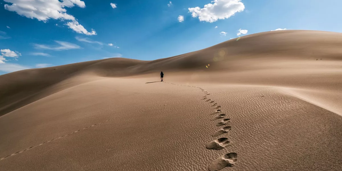 person walking along sand and leaving footprints