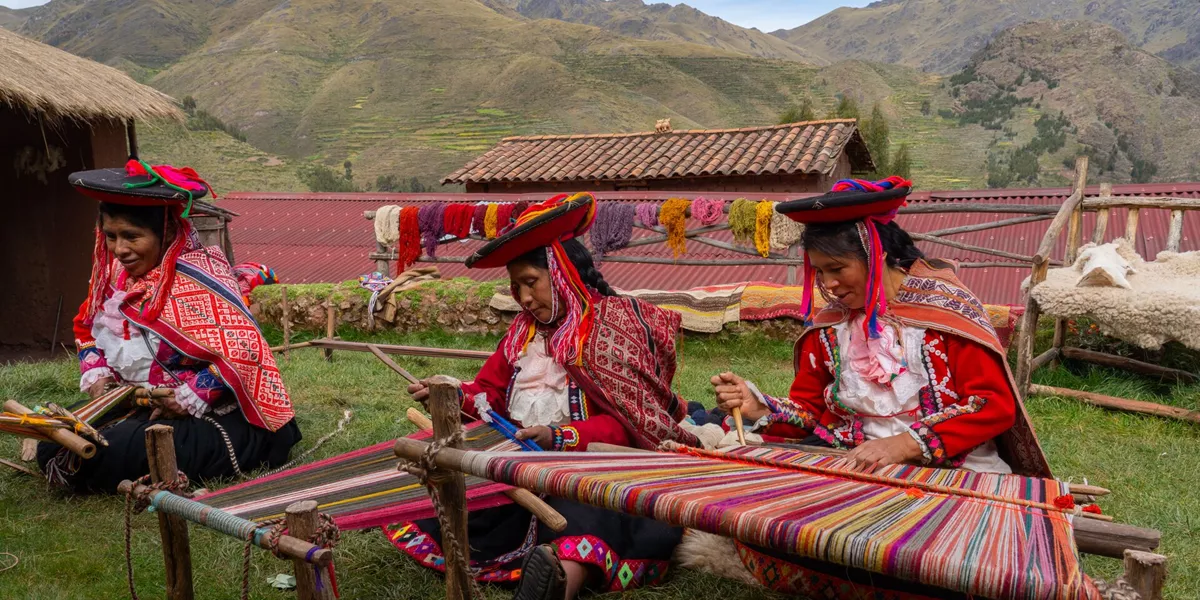 tHree Local Female Weavers In Colourful Traditional Local Dress Including Festooned Hats, Weaving Colourful Alpaca Wool On The Ground