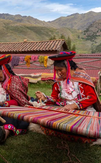 tHree Local Female Weavers In Colourful Traditional Local Dress Including Festooned Hats, Weaving Colourful Alpaca Wool On The Ground